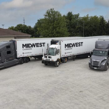 Three Midwest Carriers trucks parked in a lot with tree line in the background
