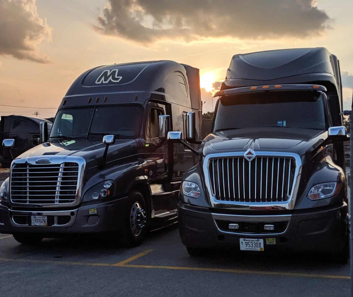 Front view of two Midwest Carriers trucks parked in the lot with the sun setting