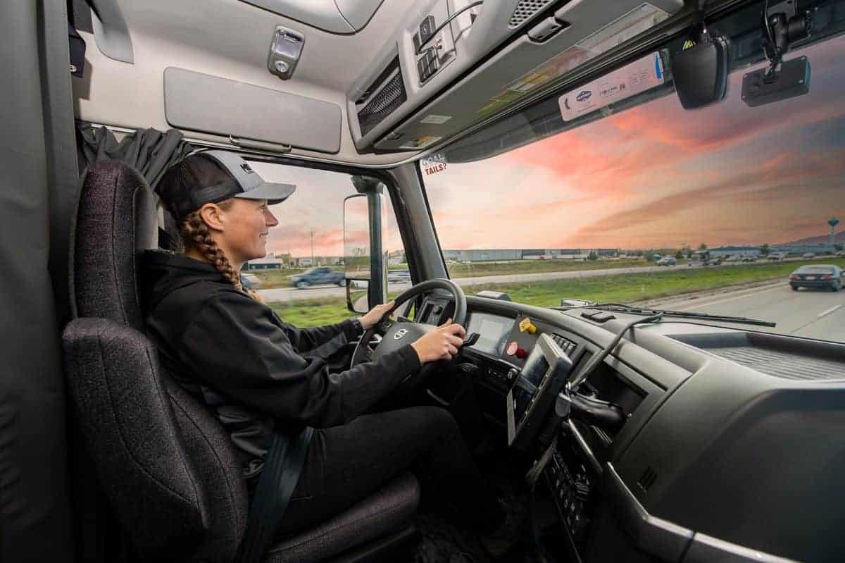 Female truck driver driving a Midwest Carriers truck down a split highway with cars driving by.