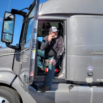 Midwest Carriers truck drivers sits in cab with door open and talking on his phone