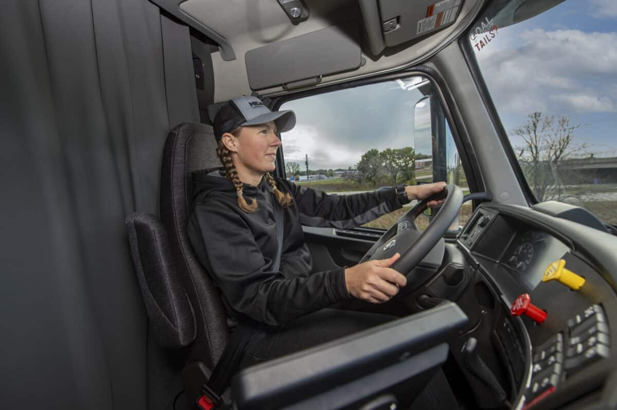 A Midwest Carriers truck driver behind the steering wheel of their truck. Outside of the truck is a rural landscape.