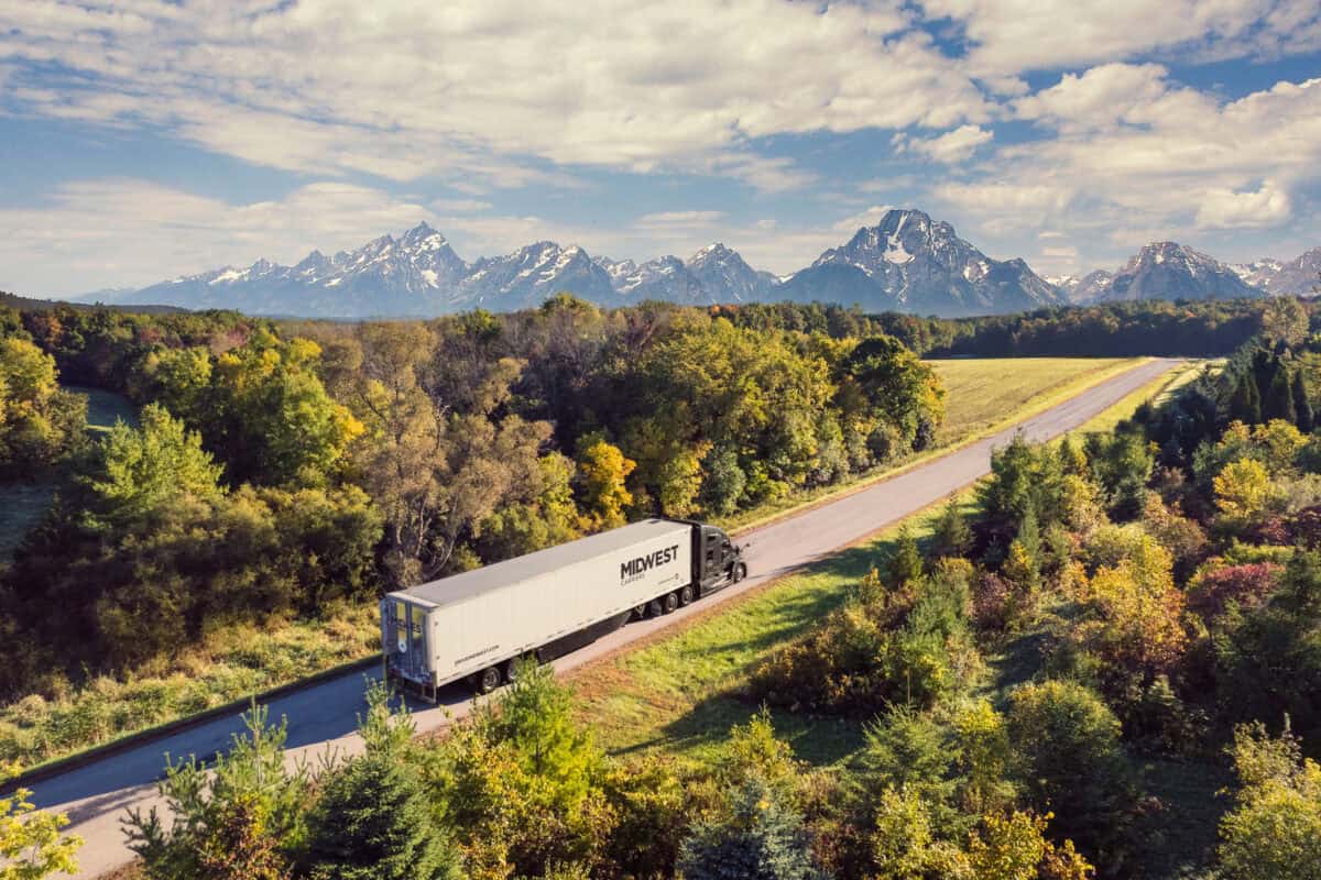 Midwest truck driving through the woods with a mountain range in the background.