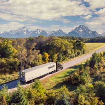 Midwest truck driving through the woods with a mountain range in the background.