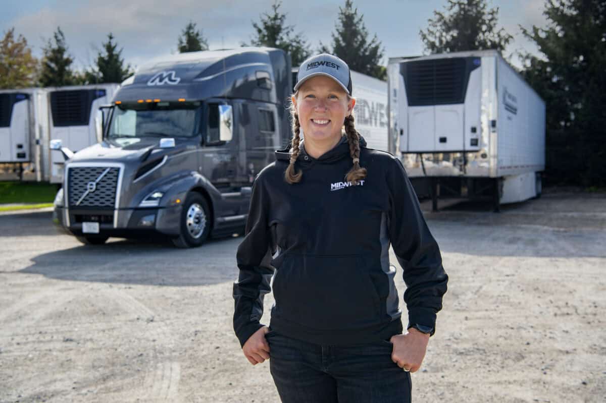 Female truck driver stand in front of Midwest Carriers truck smiling.